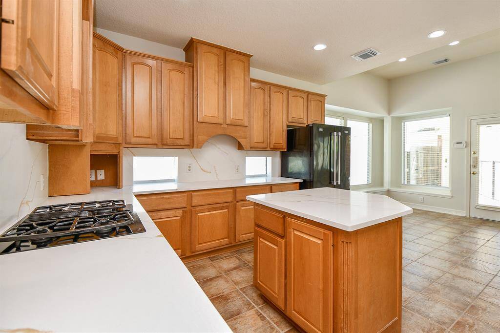 Spacious kitchen with wooden cabinetry, a central island, and modern appliances. Features a gas cooktop, plenty of natural light from large windows, and a clean, open layout.