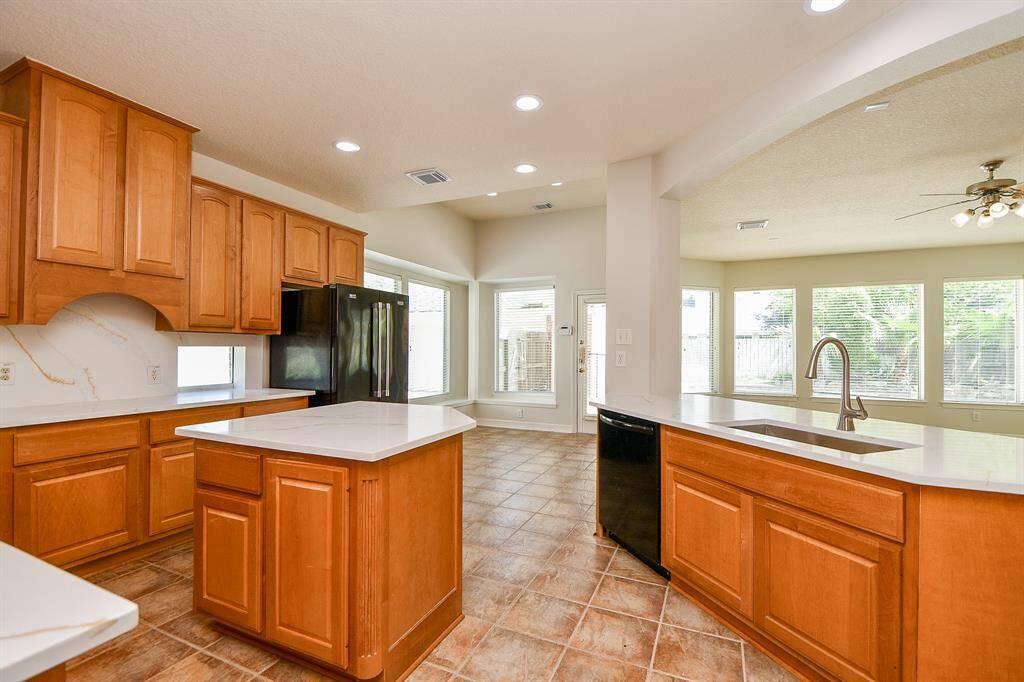 Bright and spacious kitchen with wooden cabinetry, an island, and modern appliances. It features tiled flooring, ample counter space, and large windows offering plenty of natural light.