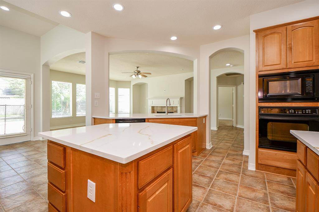 Bright, open kitchen with large island. It features ample cabinet space, recessed lighting, and a view into a spacious living area with large windows and a ceiling fan.