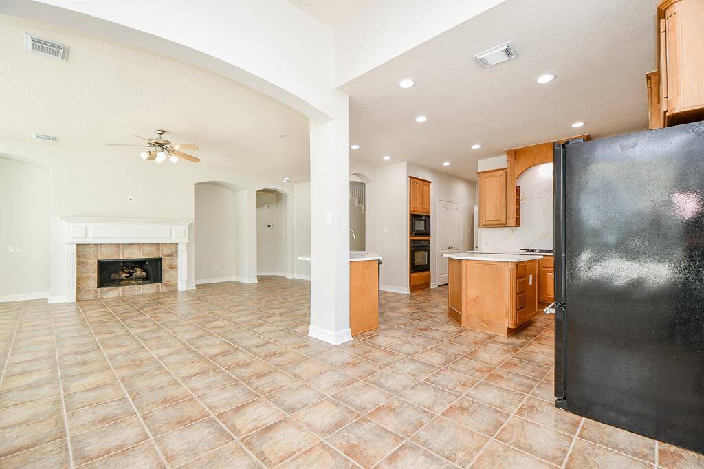 This open-concept space features a cozy fireplace, and a ceiling fan in the living area. The kitchen includes wooden cabinetry, modern appliances, and recessed lighting, creating a warm and inviting atmosphere.