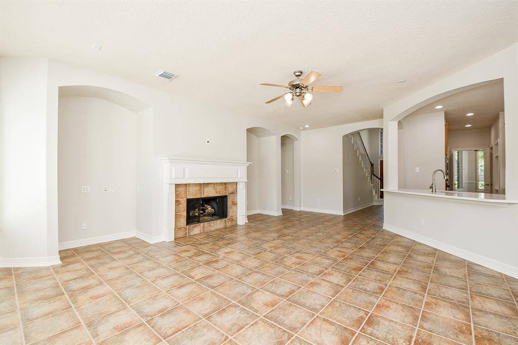 This spacious living area features a cozy fireplace, and neutral walls. It includes a ceiling fan and opens to a kitchen with a bar counter. Arched openings and recessed lighting add elegance, while a staircase leads to the upper level.