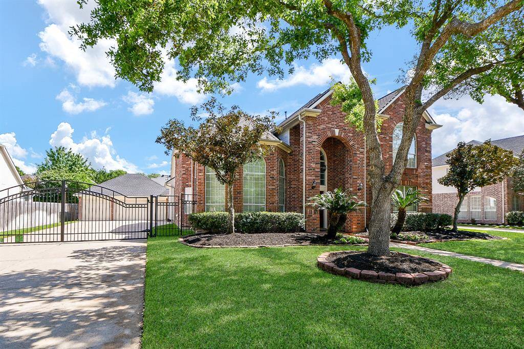 This is a beautiful brick home with a well-maintained lawn, mature trees, and elegant landscaping. It features a gated driveway leading to a detached garage, offering privacy and security. The large arched windows add charm and natural light to the interior.