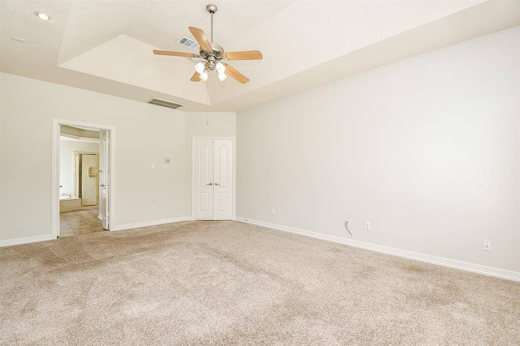Spacious primary bedroom featuring plush carpeting, elegant tray ceiling, and an ensuite bathroom for ultimate comfort and style.