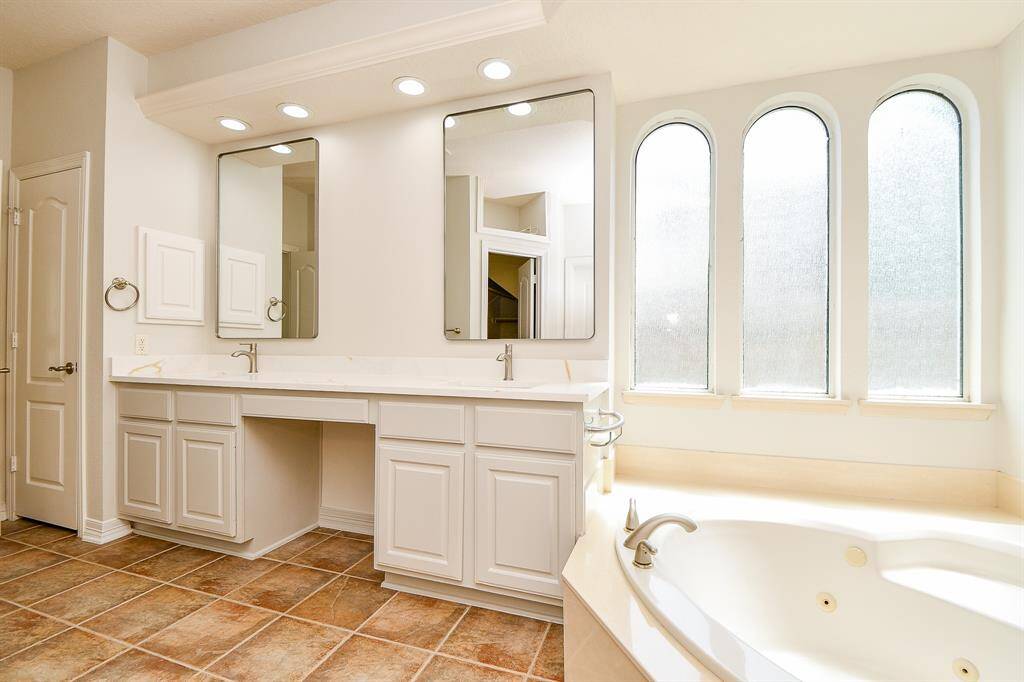 Luxurious primary bath featuring dual vanities, elegant arched windows, and a relaxing soaking tub.