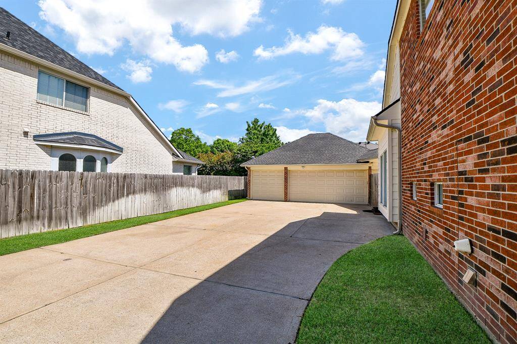 This photo showcases a spacious driveway leading to a large three-car garage, bordered by a brick house and a wooden fence, with a small patch of green grass.