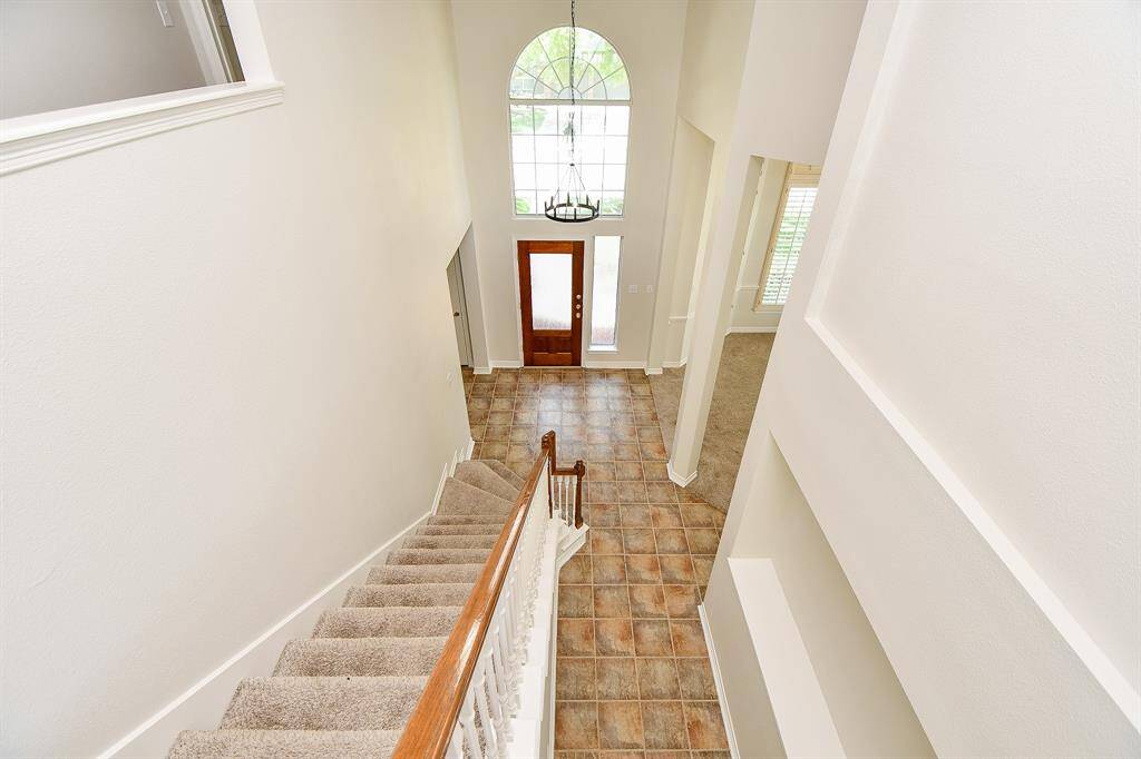This photo showcases a bright and spacious entryway with a high ceiling and large arched window above the front door. There is a welcoming atmosphere, leading into an open living area.