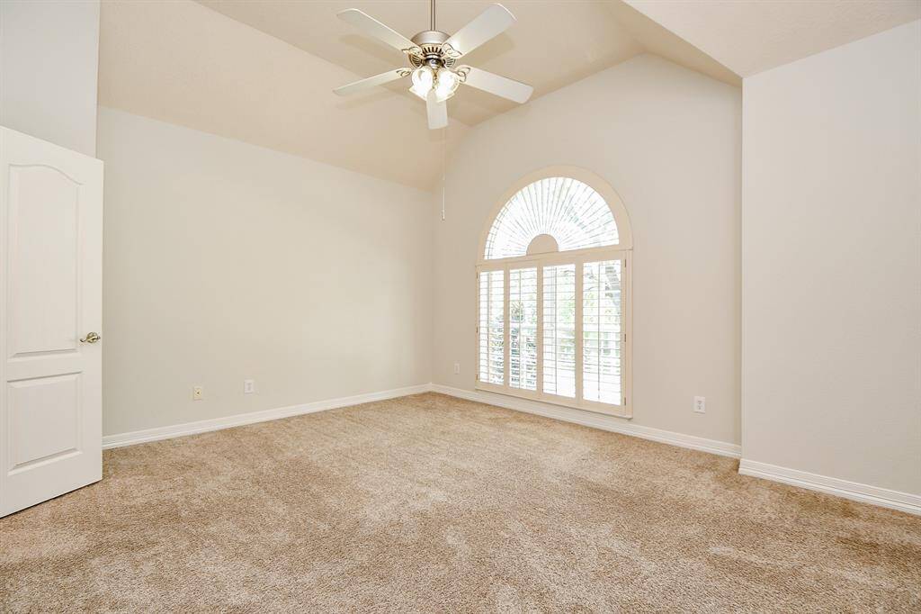 Bright and spacious secondary bedroom featuring high ceilings and a charming arched window with shutters. Perfect for a cozy retreat or versatile space.