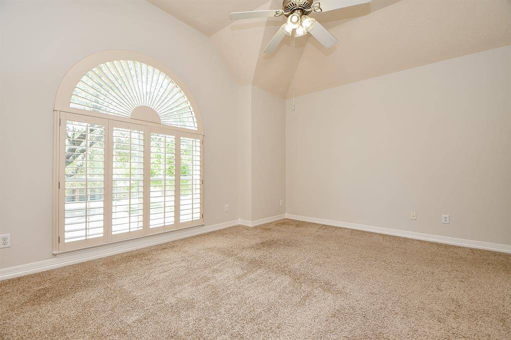 Bright and inviting secondary bedroom featuring a vaulted ceiling, elegant fan, and large arched window with plantation shutters.