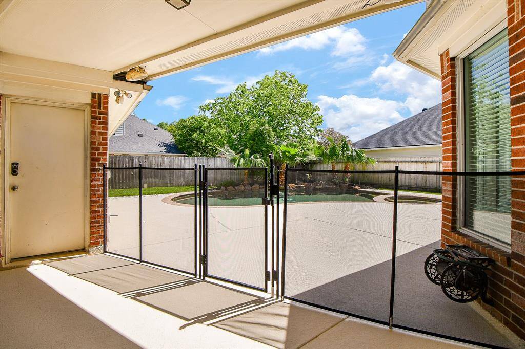 This photo showcases patio area with a secure gate leading to a spacious backyard featuring a pool. The space is surrounded by a privacy fence and includes a mix of grass and landscaping, creating a relaxing outdoor environment.