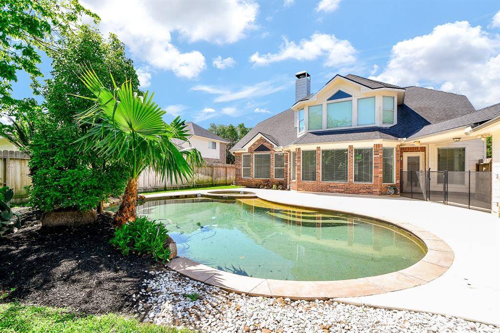 This photo showcases a bright backyard featuring a home with large windows and a stylish pool surrounded by lush greenery.