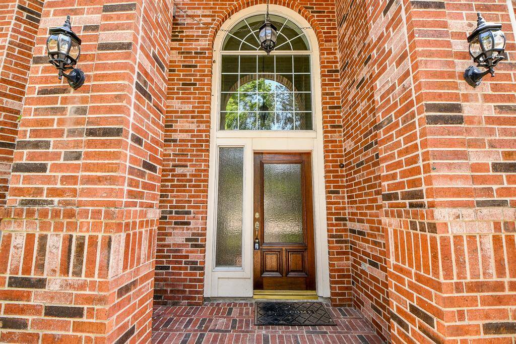 This photo showcases a grand brick entrance with a wooden door, sidelights, and an arched window above. Flanked by decorative wall lanterns, it offers a classic and welcoming feel.