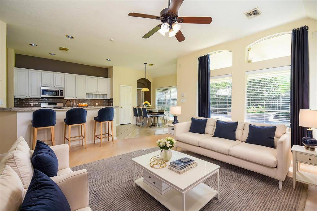 The open-concept family room, kitchen, and breakfast nook flow seamlessly together, creating a warm and connected living space. The kitchen features a breakfast bar with bar stools, perfect for casual dining. Large windows fill the space with natural light and offer views of the backyard, making it ideal for everyday living and entertaining. Virtually Staged Photo