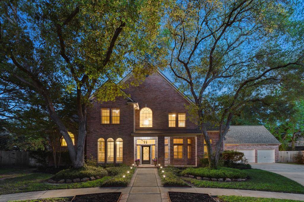 Welcome to 23007 Meadow Pond Cir, where soft evening light highlights the elegant brick exterior and charming walkway beneath a canopy of mature trees.