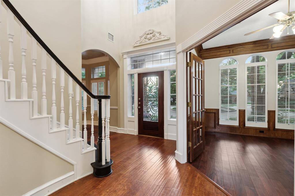 Dramatic entry with tall ceilings, wood flooring, and staircase view.