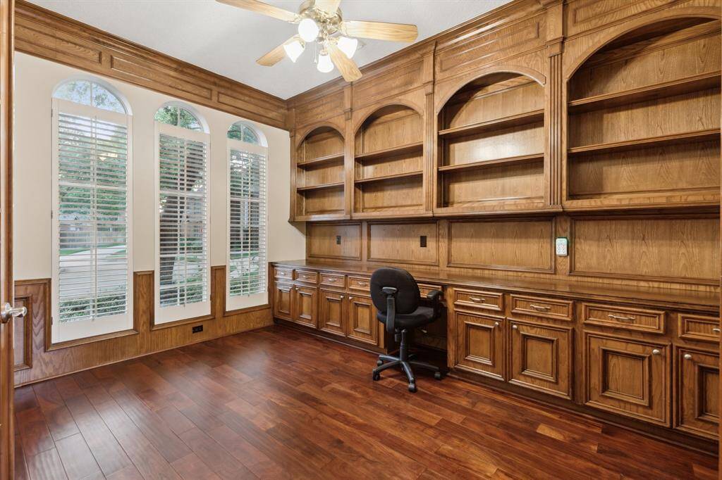 Custom-built library shelving and desk with large shuttered windows.