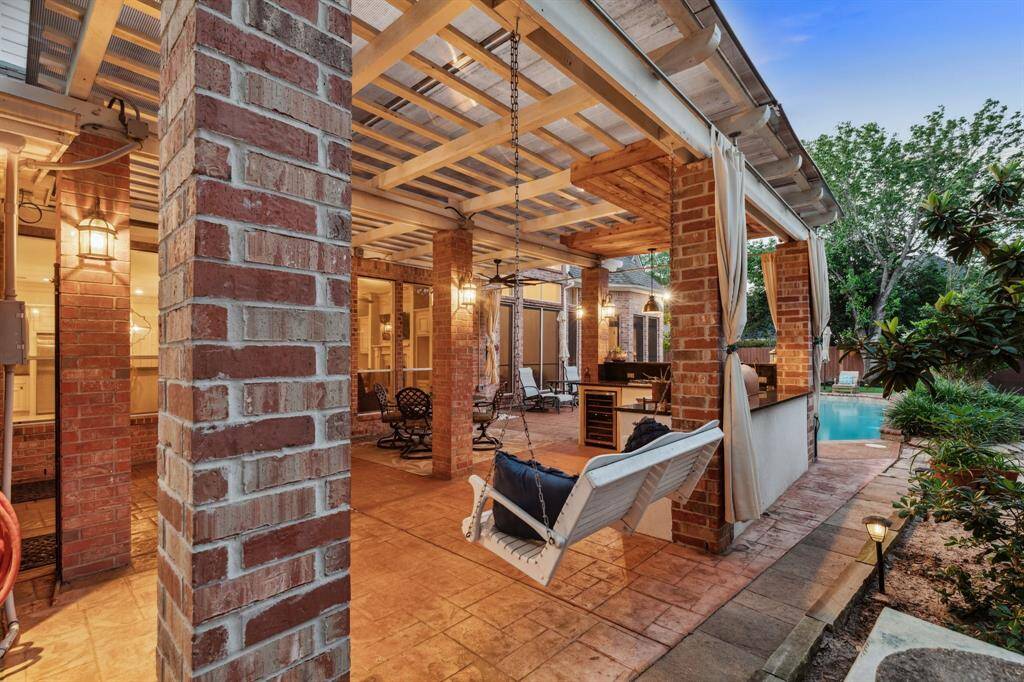 Inviting covered patio with a hanging swing, brick columns, and soft lighting.