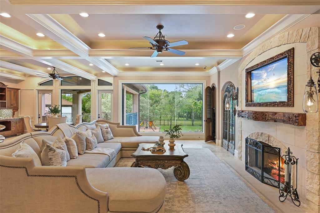 Step inside to a sun-filled living room with floor to ceiling windows, illuminated trayed ceilings, stone gas log fireplace with antique wood-carved mantle & closet to house all media components.