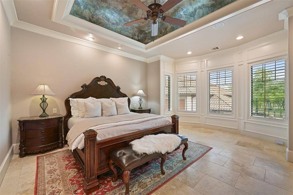 The primary suite offers a luxurious & grand space to enjoy sweeping views outdoors, a lavish trayed ceiling with one-of-a-kind details, plantation shutter & book shelf built-ins.