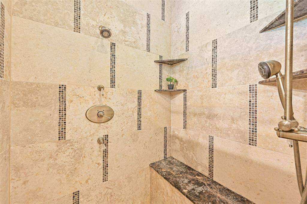 The large walk-in shower features multiple shower heads, granite shaving & accessory ledges.