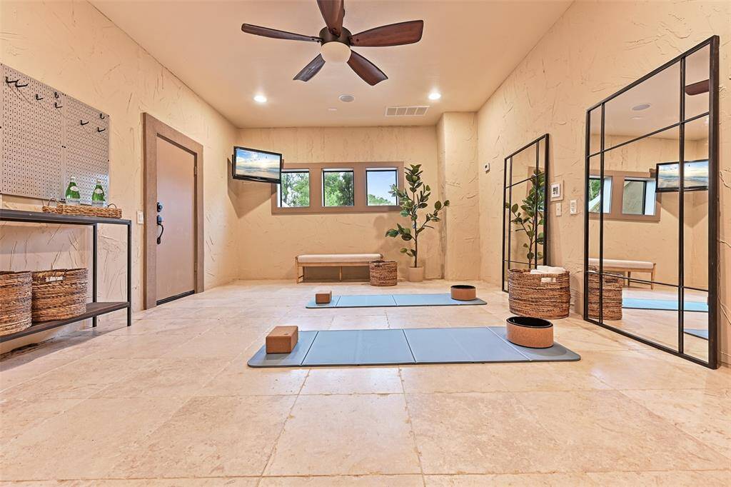 A zen-like exercise room with stone flooring, wall mounted tv, and nearby access to a full bathroom provide the perfect setting for a home gym. Tucked behind the closet door is a large storage area with shelving to store holiday decorations, table & chairs for hosting large events and more.