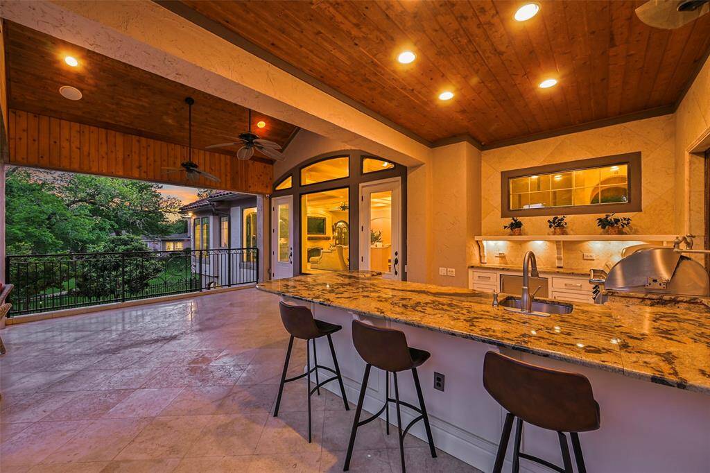 An exquisite summer kitchen with abundant granite countertops offering plenty of space for serving and meal preparation. Grill, sink, separate burner for boiling, beverage fridge, cabinetry, functional antique shutters, sound system, outdoor fans and lighting make an exception space for entertaining.