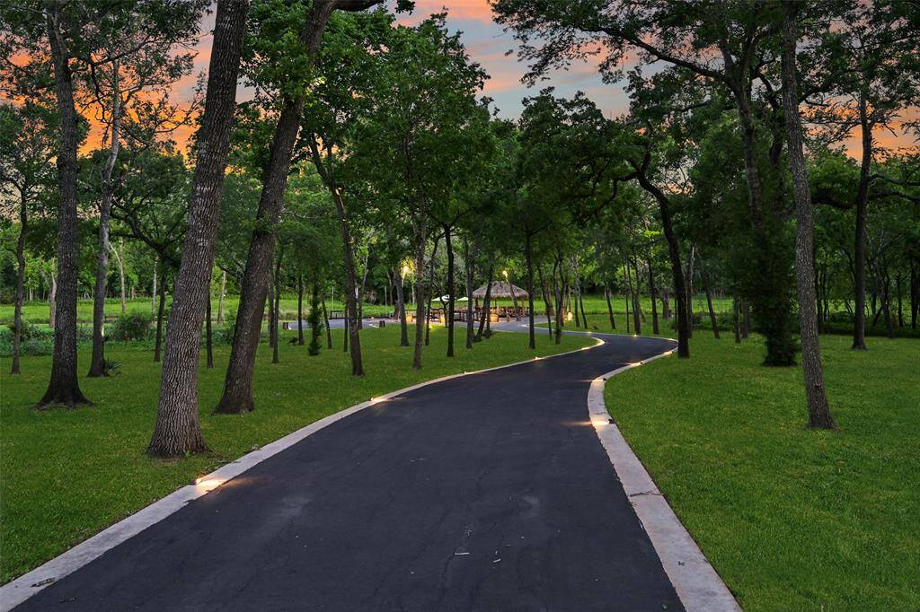 A winding, black-top road, outlined by outdoor lighting, makes it way through the trees to the outdoor waterfront entertaining space.