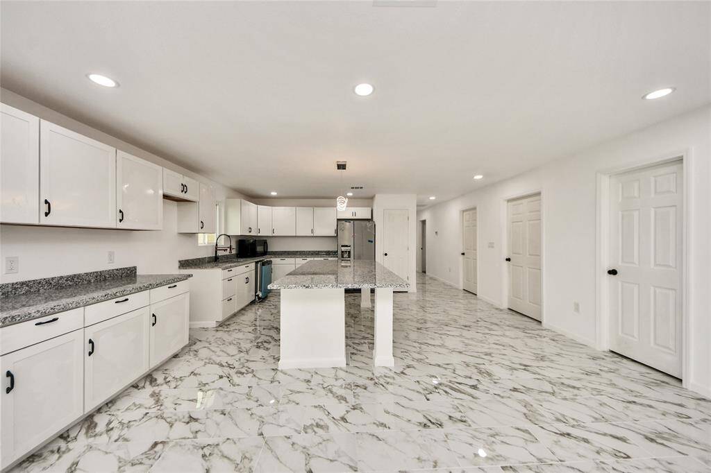 Chef’s dream kitchen boasting an oversized granite island, ample white cabinetry with matte black hardware, and brand-new stainless-steel appliances.