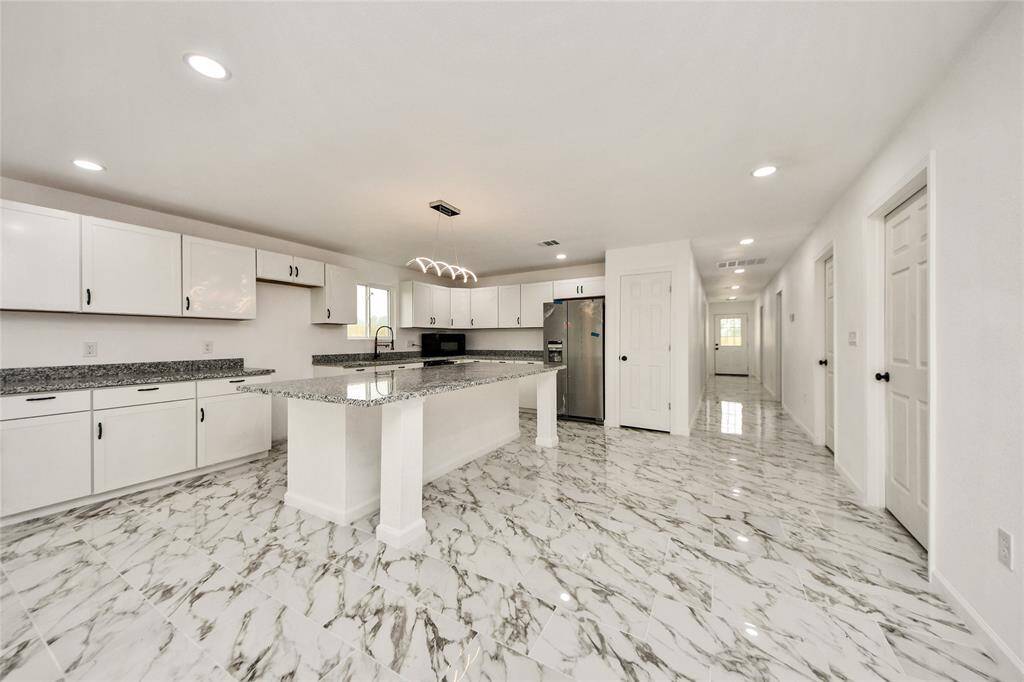 Another view of the modern kitchen showcasing the stylish light fixture above the island and the wide, open layout perfect for entertaining.