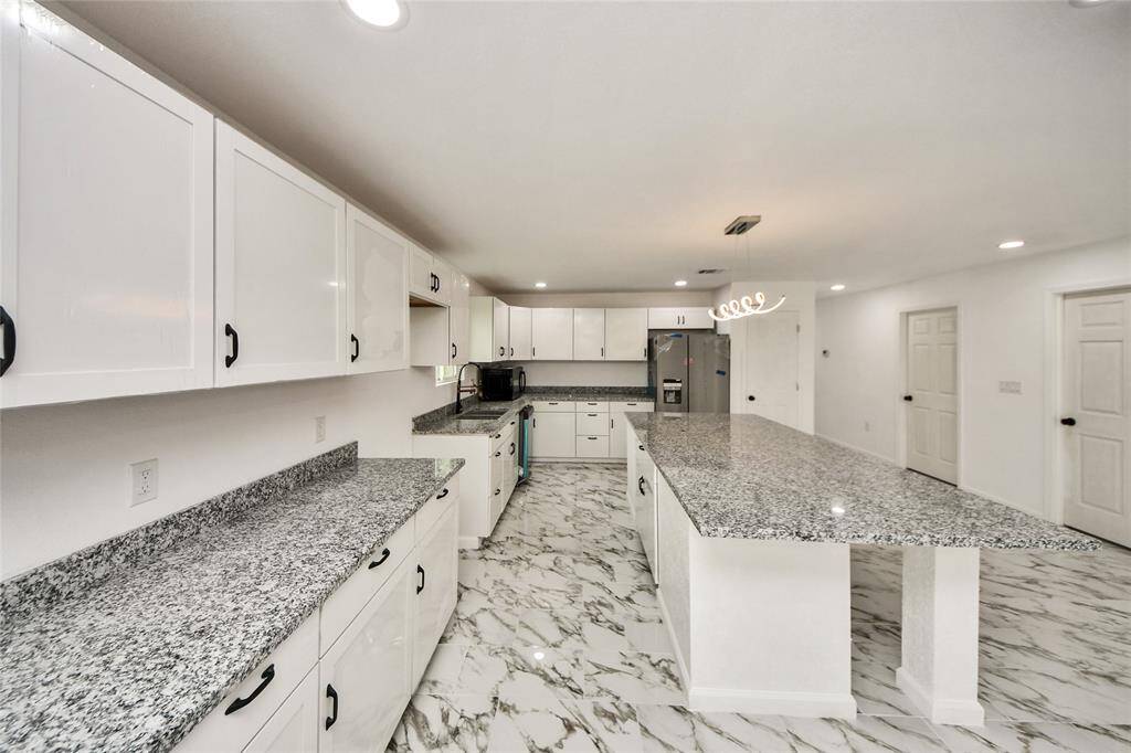 Detailed view emphasizing the gorgeous granite countertops, plentiful white cabinetry, and the fresh, modern finishes throughout the kitchen.