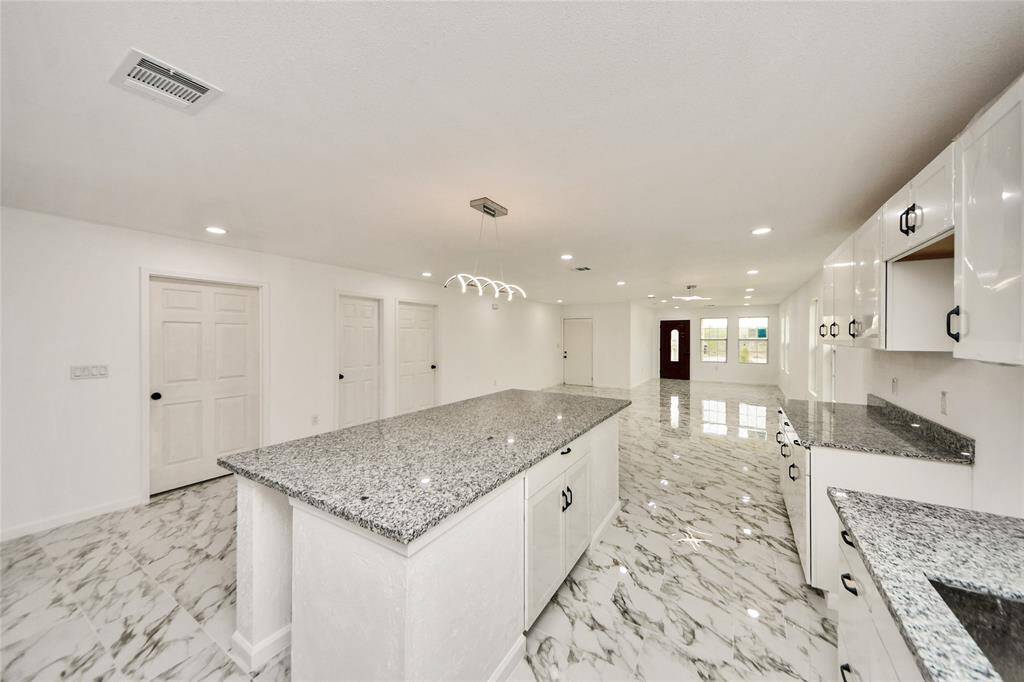 A reverse angle highlighting the connection between the large kitchen island and the open living space, with sightlines clear from the kitchen to the front door.