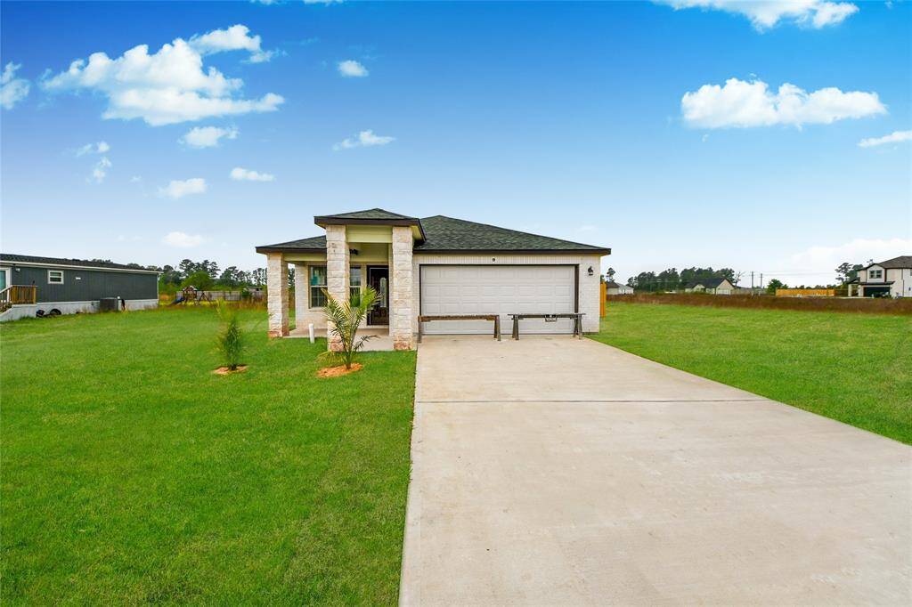 Bright, inviting front view of the home with a charming stone-accented porch, fresh landscaping, and an expansive driveway leading to a two-car garage.