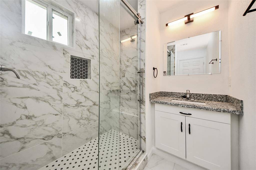 Luxurious walk-in shower with floor-to-ceiling marble-look tile and a built-in niche, accented by a glass door.
