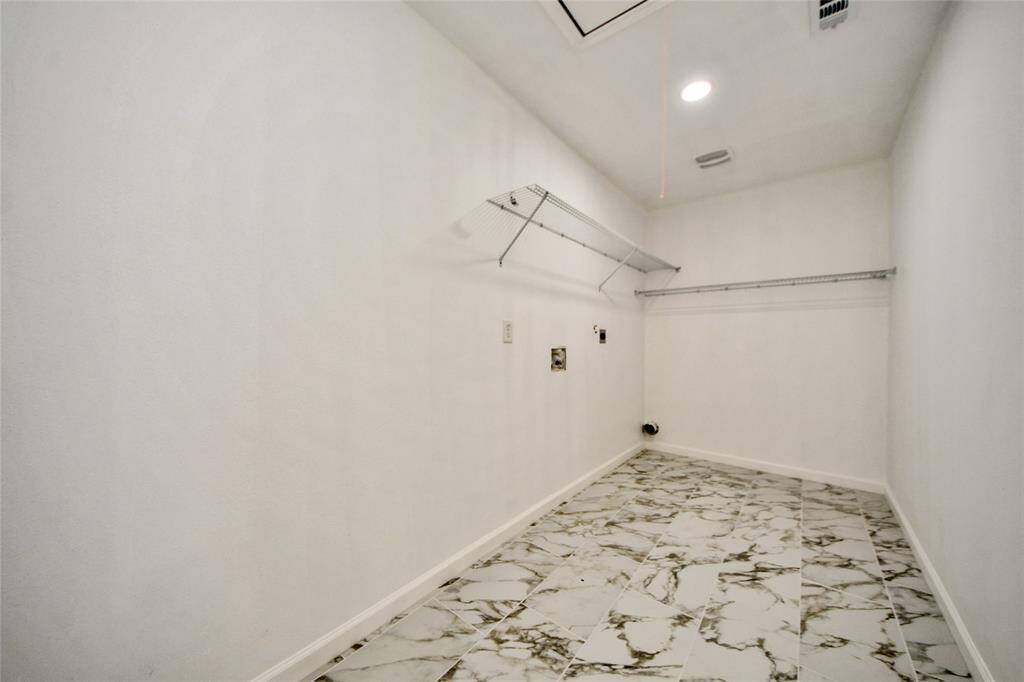 Oversized laundry room with marble-look tile flooring, shelving, and connections for washer and dryer.