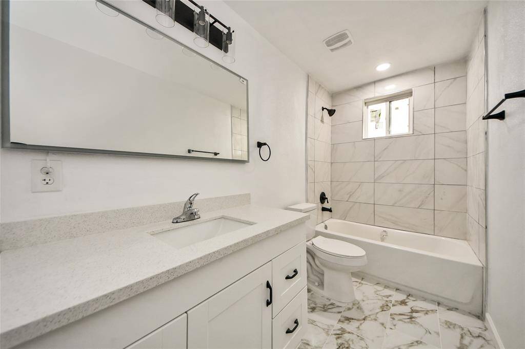 Stylish hall bathroom with modern finishes, including a sleek white vanity, quartz countertop, updated fixtures, and a beautifully tiled shower and tub combo.