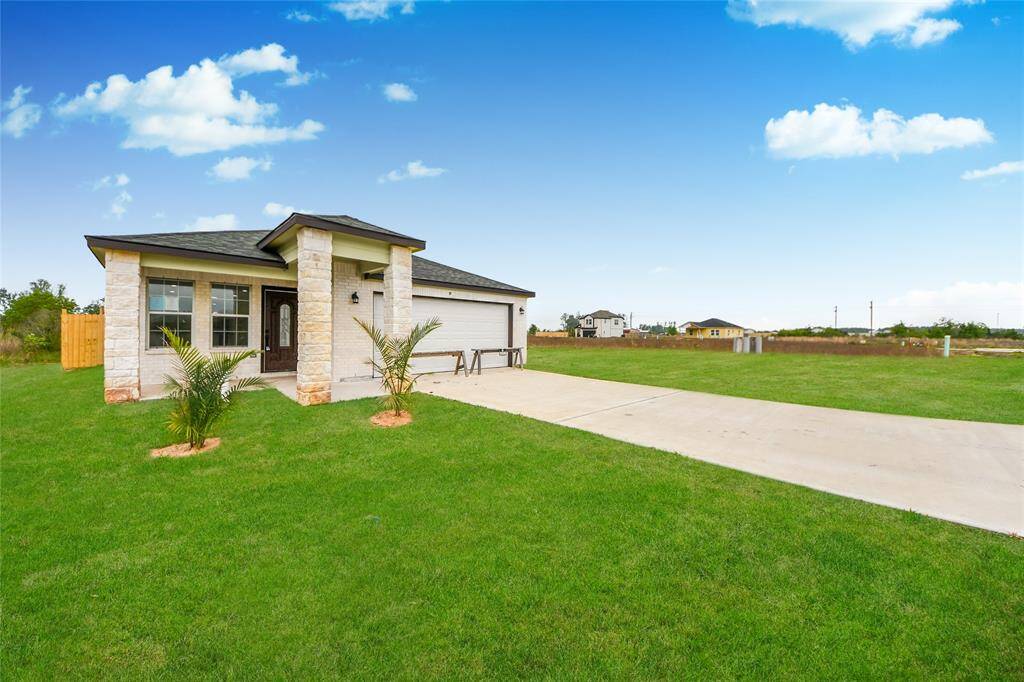 Angled daytime exterior view showcasing the welcoming covered front porch, dual stone columns, and the wide green lawn offering plenty of outdoor space.