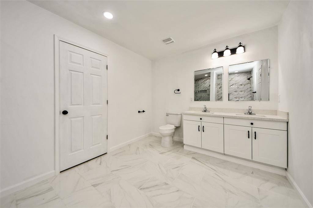 Spa-like primary bathroom featuring dual vanities, framed mirrors, a private toilet area, and stunning marble-look tile flooring throughout.