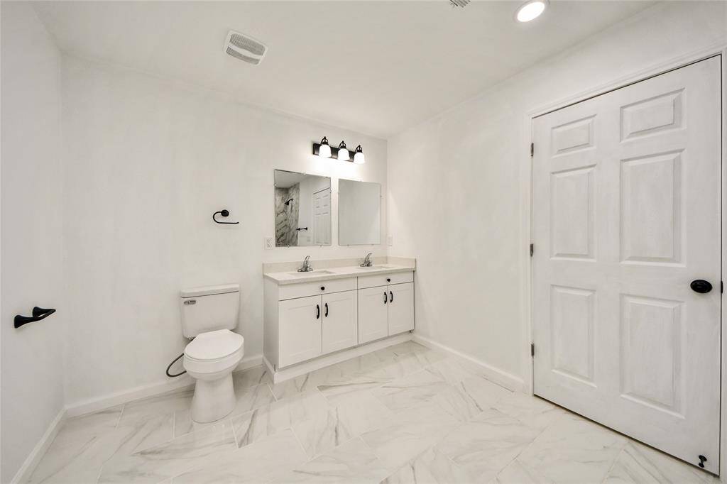 Another view of the spacious primary bath highlighting the generous layout, dual sinks, and stylish light fixtures.