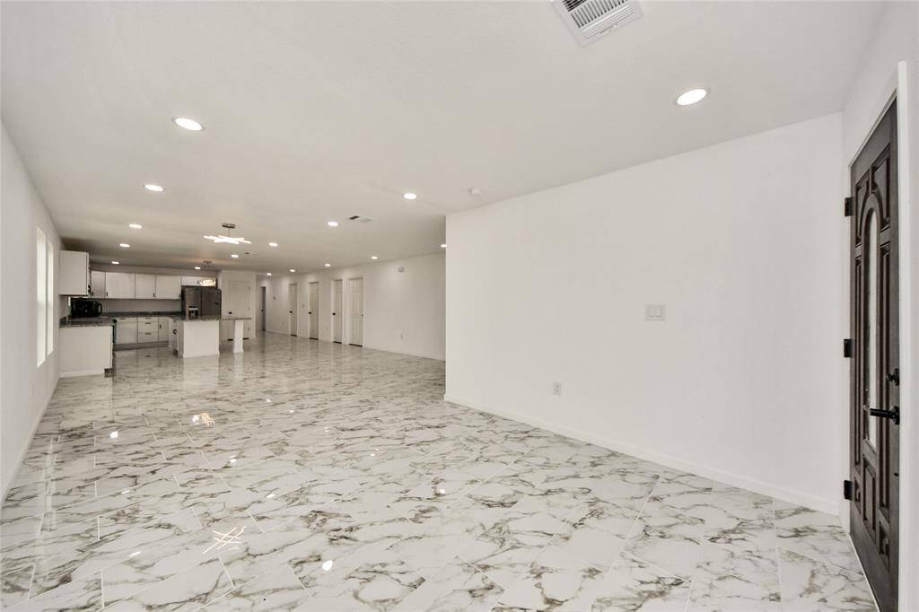 A view from the entryway into the open-concept living space featuring polished marble-look tile floors, recessed lighting, and neutral tones for a bright, airy atmosphere.