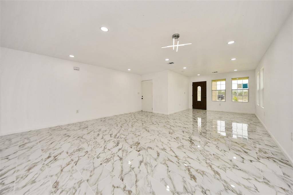 Another angle of the open living area with large windows allowing natural light to flood the space, highlighting the modern front door and sleek interior finishes.