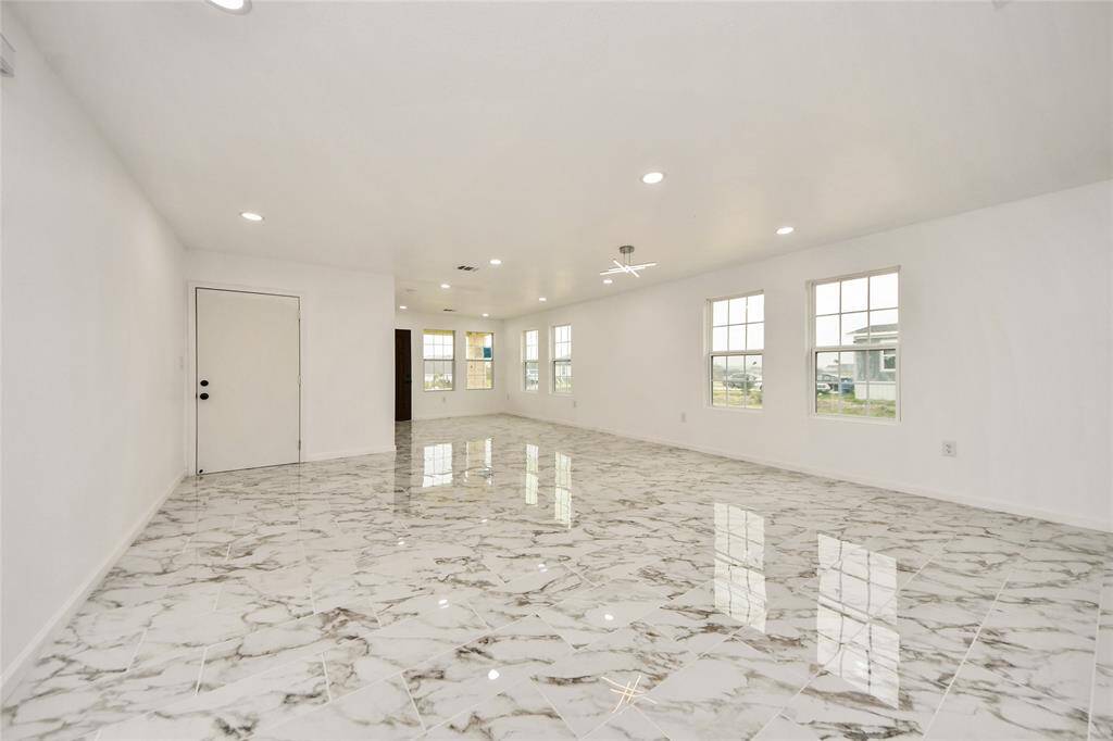 A perspective from the back of the living space emphasizing the vast layout, glossy marble-style flooring, modern lighting fixtures, and abundance of natural light.