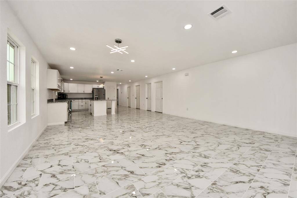 Spacious open floor plan combining the living and kitchen areas, featuring stunning marble-look tile flooring, recessed lighting, and sleek modern fixtures.