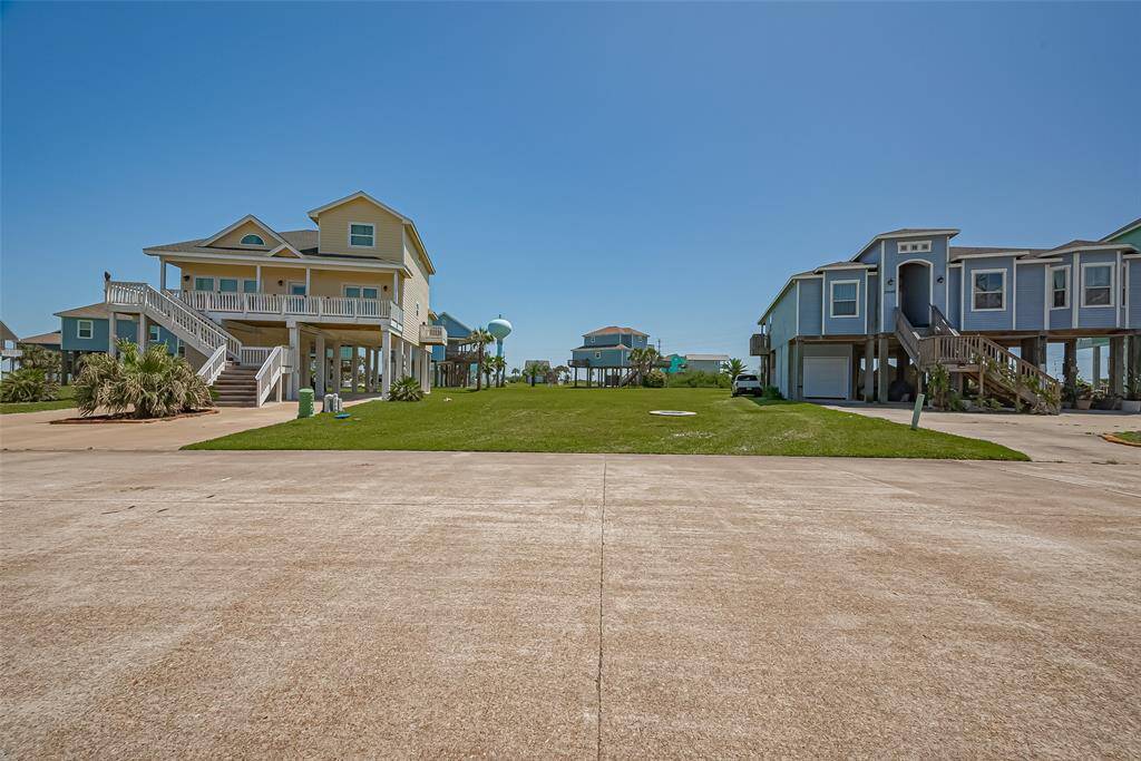 A gentle ground-level perspective reveals the pristine lot framed by neighboring coastal architecture, the manicured grass lending a peaceful rhythm to the serene streetscape.