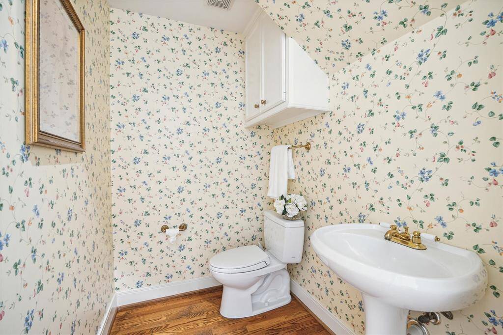 This charming powder bath features floral wallpaper, a pedestal sink with brass fixtures, just a classic look. Hardwood floors add warmth, while a wall cabinet provides storage. A wonderful space with vintage charm.