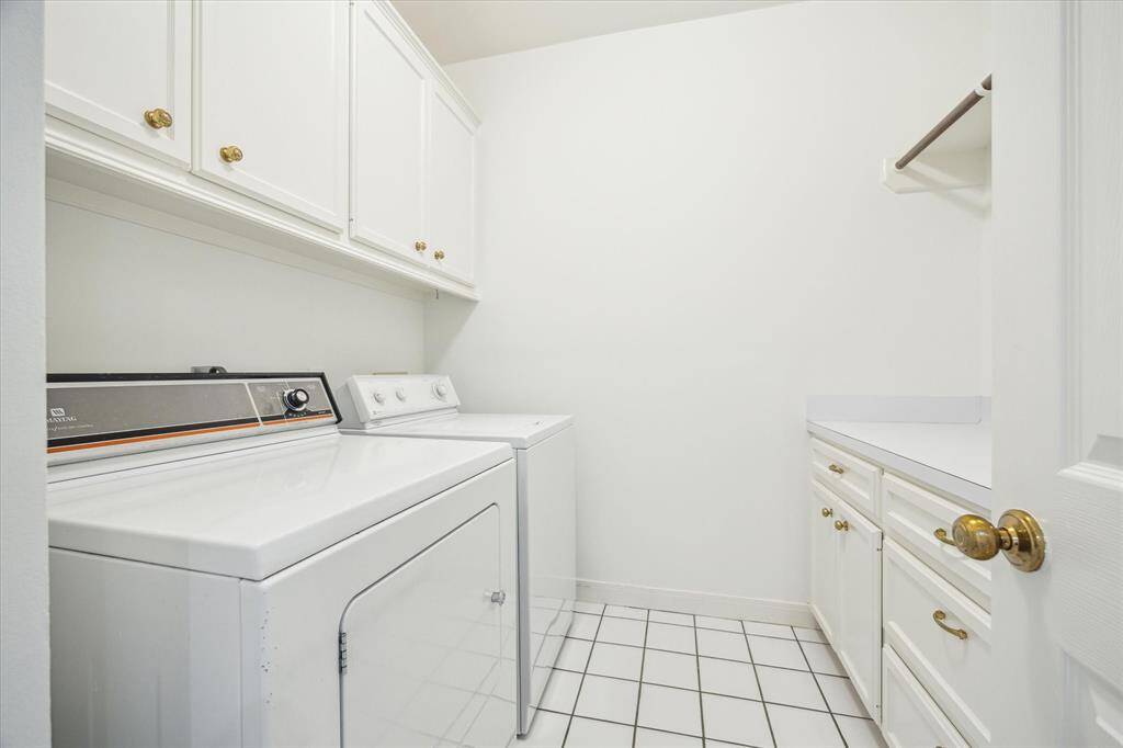 This photo shows a bright, functional laundry room with a washer and dryer, ample cabinet storage, a countertop for folding, and a tiled floor.