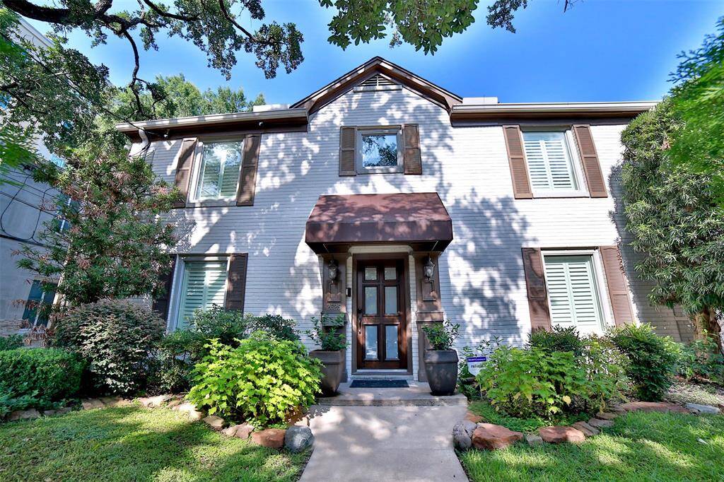 This charming two-story home features a classic brick exterior with elegant shutters and a welcoming front porch. The lush landscaping and mature trees create a serene and inviting atmosphere, perfect for enjoying outdoor living.