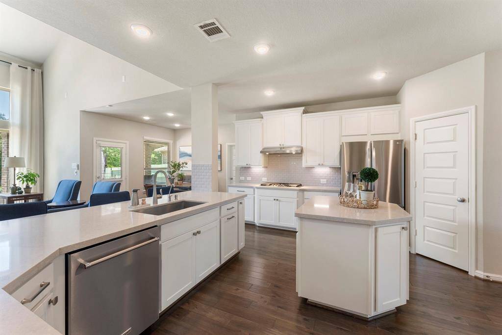 A modern kitchen with white cabinetry, island, and breakfast bar. The 3 car tandem garage offers two entry doors one into kitchen and another at breakfast room.