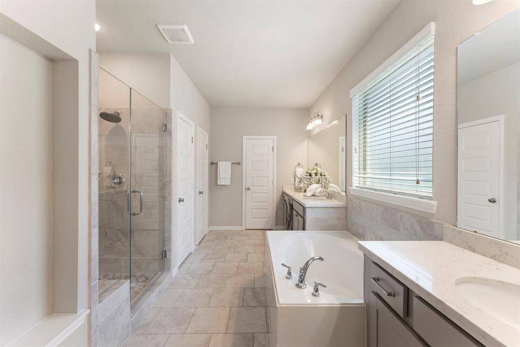 This beautiful primary bathroom features an upgraded luxury frameless shower door, a large soaking tub, and double sinks with very spacious countertops.  Large closet at rear and linen closet on left.