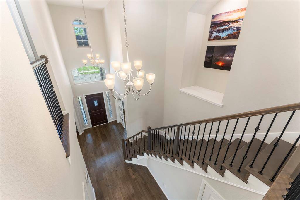 A bright, spacious foyer with high ceilings, elegant chandelier, and a wooden staircase with iron railings..