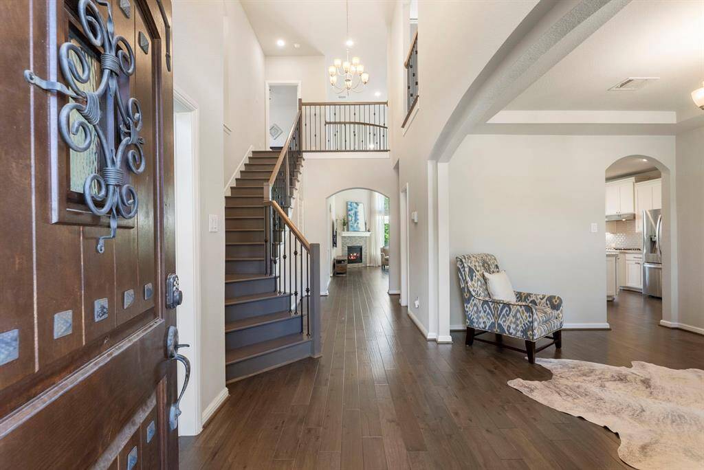 This inviting home features a grand entrance with a beautiful wood door, leading to an open foyer with high ceilings and elegant wood & iron staircase. The space is bright and airy, with hardwood floors throughout first floor including primary bedroom. The kitchen and living area are visible, offering a glimpse of modern appliances and comfortable living spaces. Perfect for those seeking style and functionality.