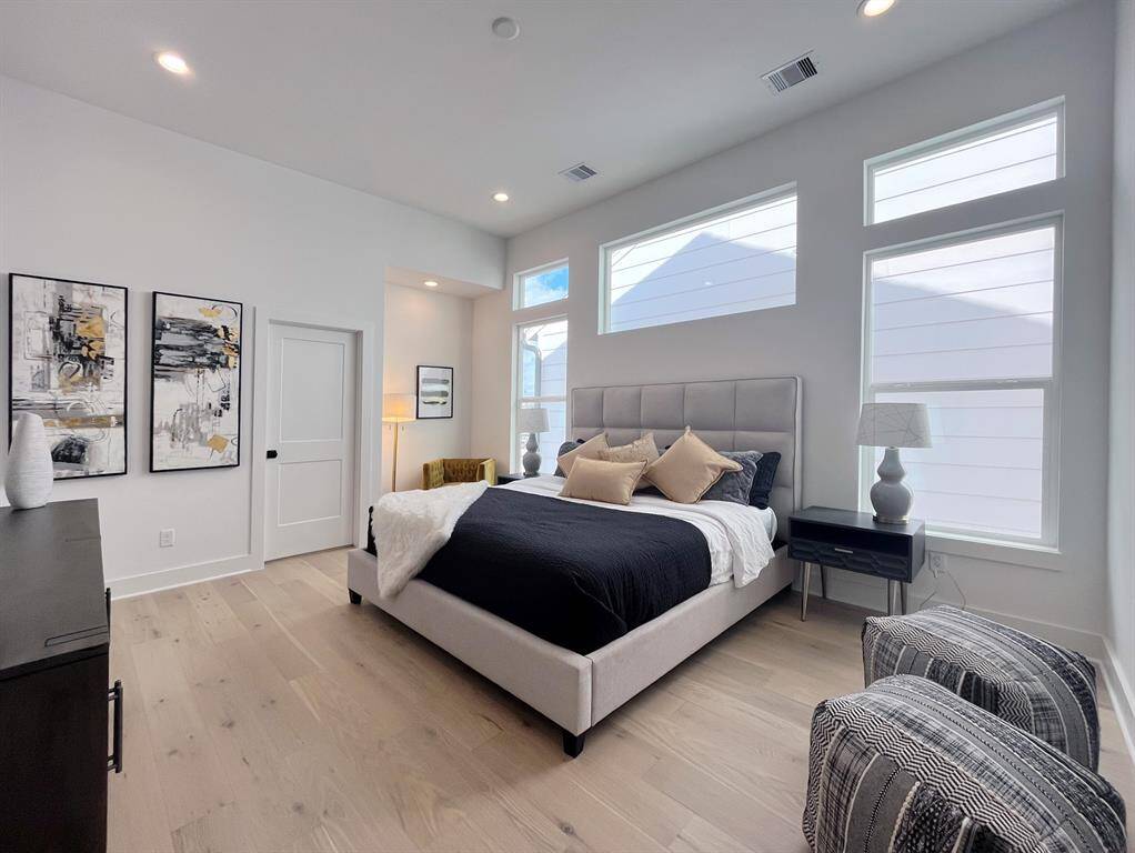 Luxurious primary bedroom featuring abundant natural light, sleek hardwood floors, and elegant modern decor for a serene retreat.